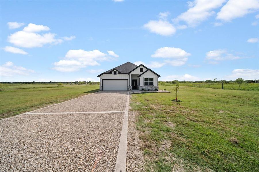 View of front of house featuring a garage, a front lawn, and a rural view