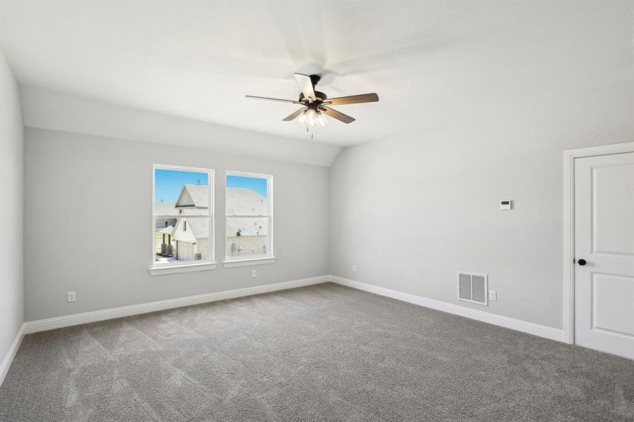 Carpeted spare room featuring vaulted ceiling and ceiling fan