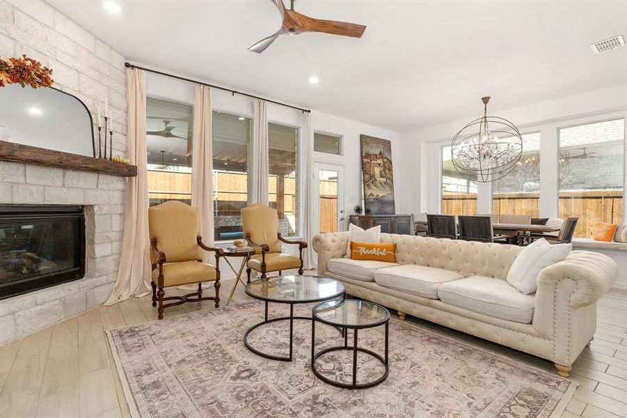 Living room featuring a stone fireplace, light hardwood / wood-style flooring, and ceiling fan with notable chandelier