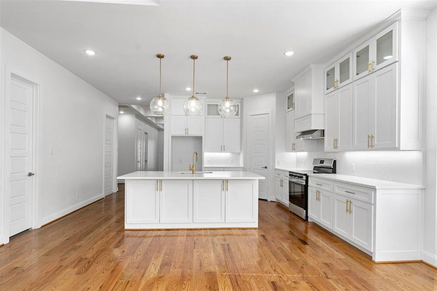 Kitchen featuring stainless steel range oven, light hardwood / wood-style flooring, a kitchen island with sink, white cabinets, and pendant lighting