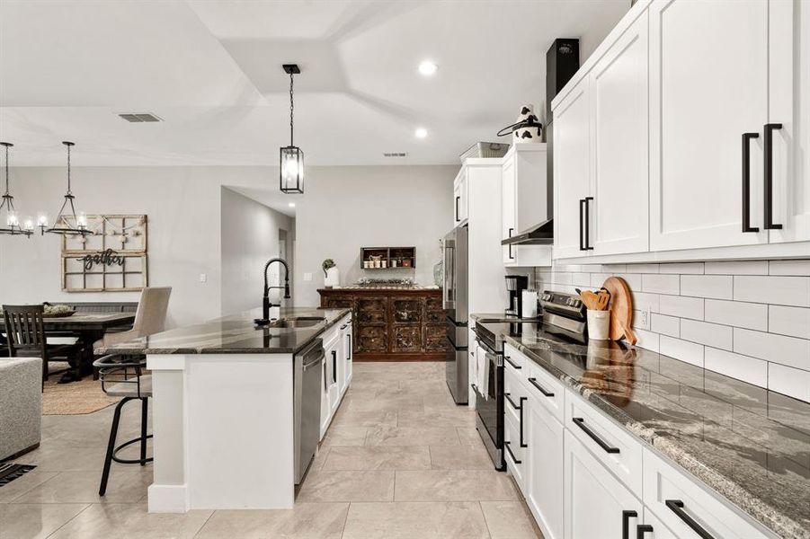 Kitchen with light tile flooring, stainless steel appliances, granite countertops and decorative backsplash.
