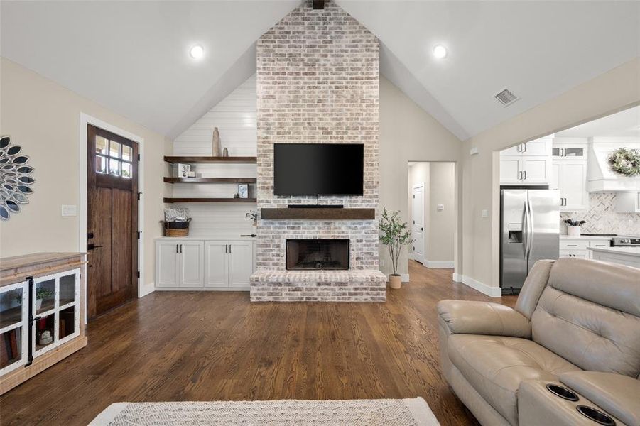 Living room with brick wall, a brick fireplace, and dark hardwood  floors