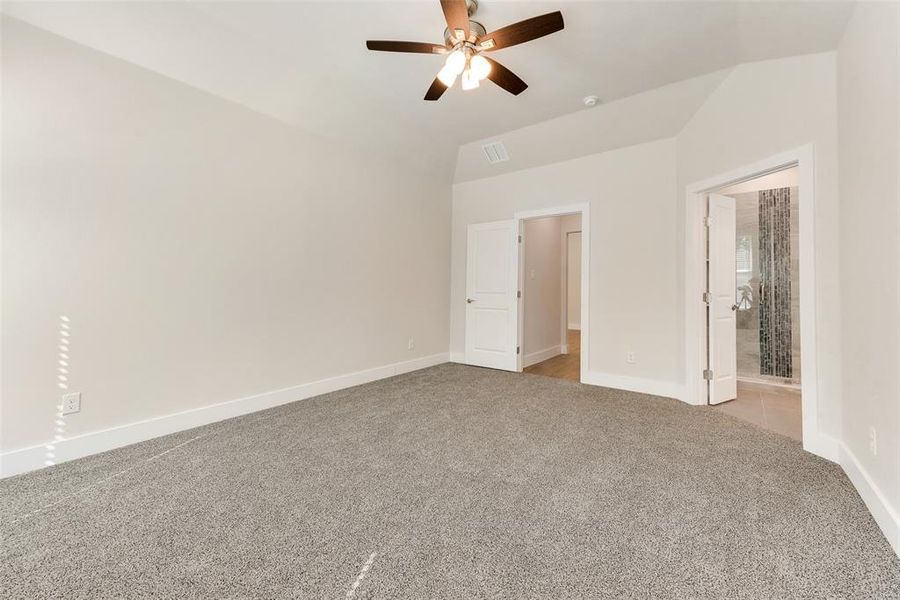 Unfurnished bedroom with vaulted ceiling, ceiling fan, light colored carpet, and ensuite bathroom