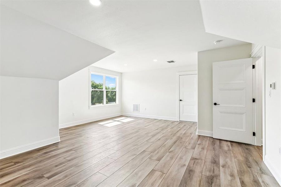 Additional upstairs living space with vaulted ceiling and light hardwood / wood-style floors