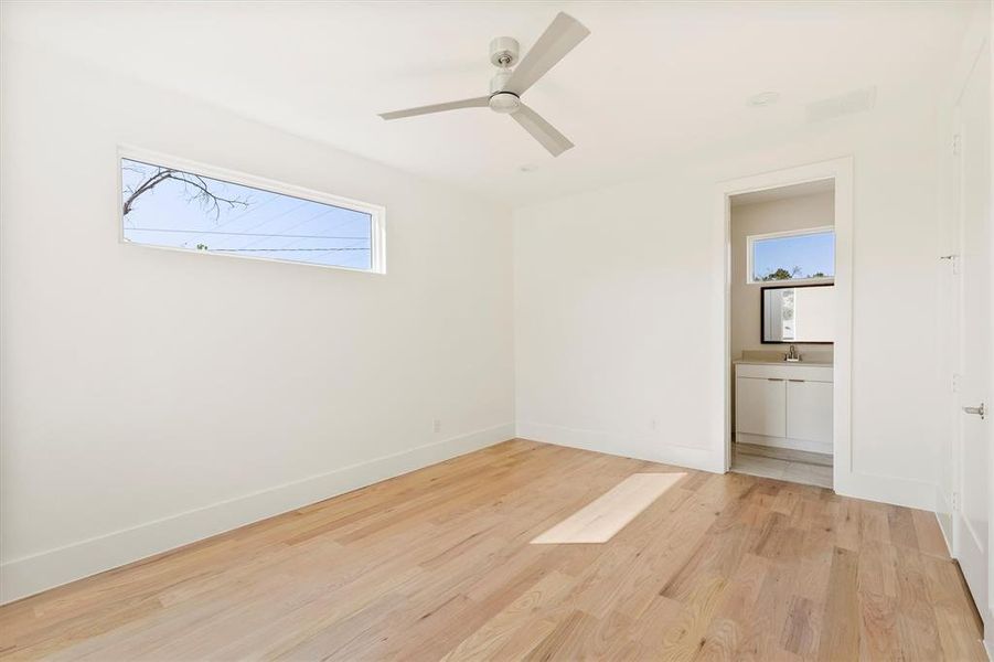 Unfurnished bedroom featuring light wood-type flooring, connected bathroom, multiple windows, and ceiling fan