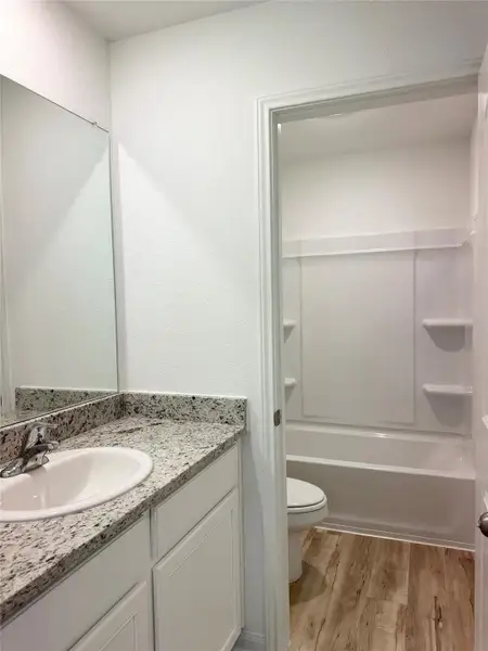 Secondary bathroom includes granite counters, designer white cabinetry and luxury vinyl plank flooring.