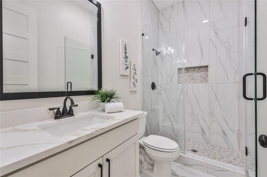 Second bathroom with frameless step in shower with pebble flooring & Quartz counter on vanity.