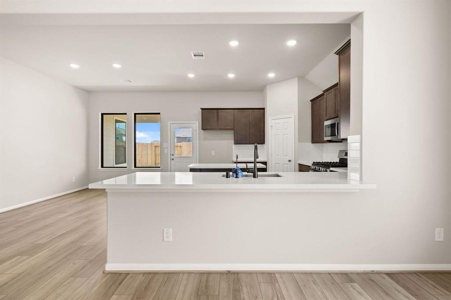 This light and bright kitchen features a large quartz island, dark stained cabinets, a large sink overlooking your family room, recessed lighting, and beautiful backsplash.