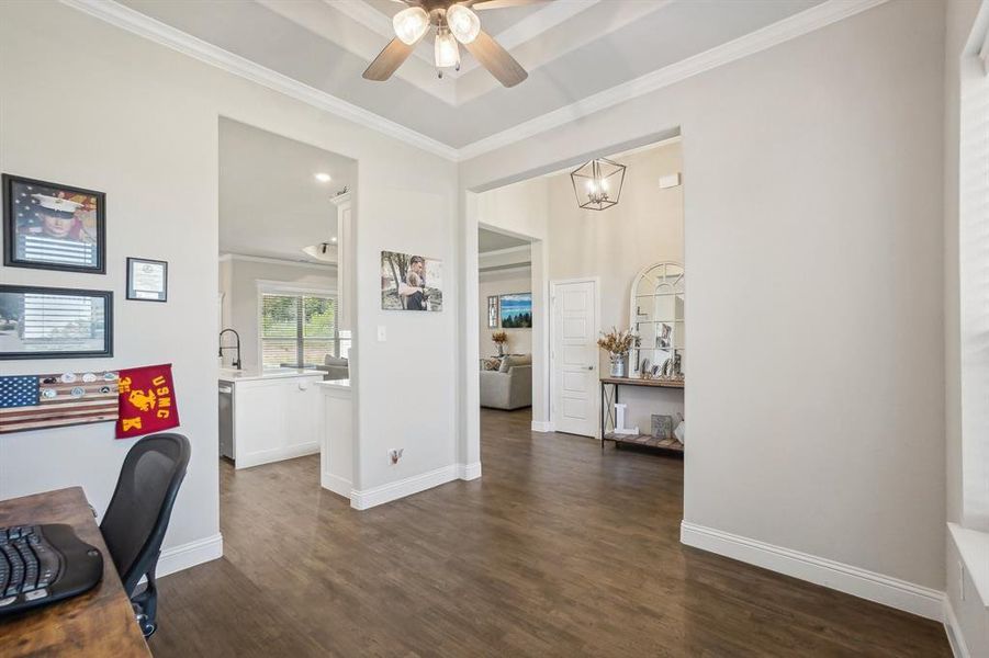 Home office with ceiling fan with notable chandelier, ornamental molding, sink, and dark wood-type flooring