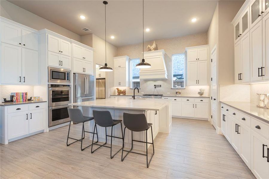 Kitchen featuring appliances with stainless steel finishes, an island with sink, white cabinets, a kitchen bar, and decorative light fixtures