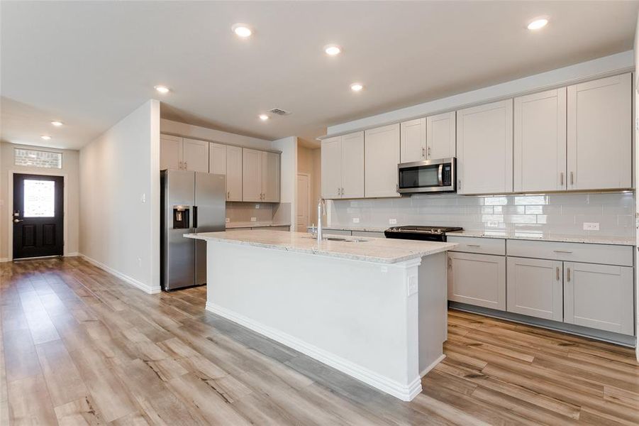 Kitchen with a center island with sink, light stone counters, luxury vinyl flooring, tasteful backsplash, and appliances with stainless steel finishes