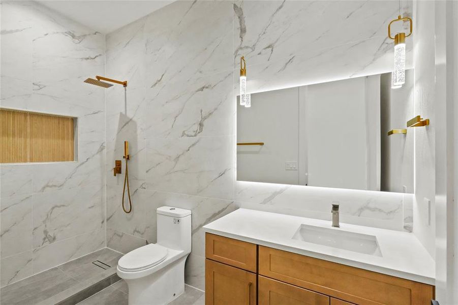 Bathroom featuring tile walls, vanity, a tile shower, and toilet