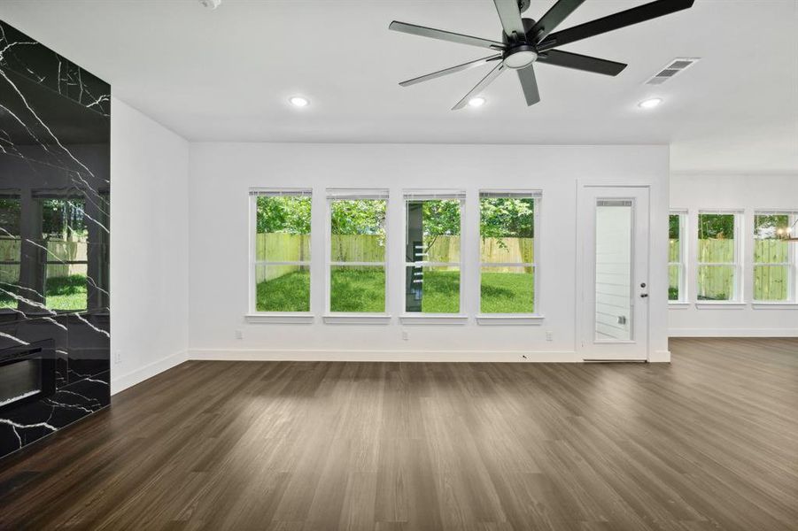 Unfurnished living room featuring a wealth of natural light, dark wood-type flooring, and ceiling fan