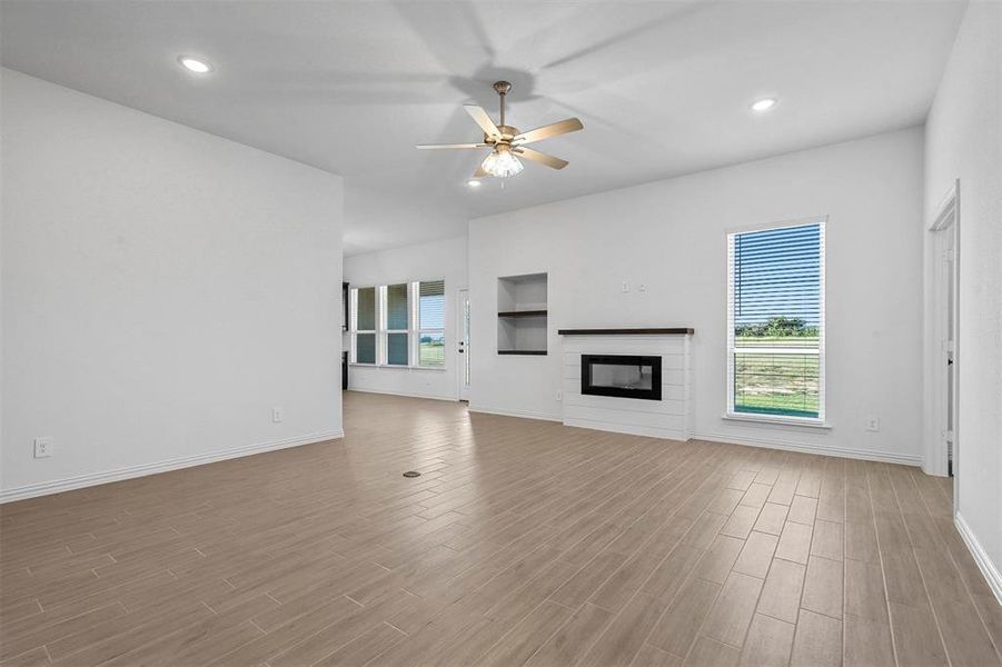 Unfurnished living room featuring ceiling fan, a wealth of natural light, and light wood-type flooring