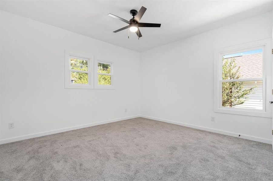 Empty room featuring carpet floors, ceiling fan, and a wealth of natural light