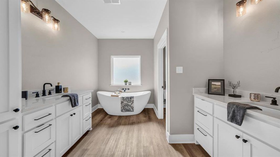 Bathroom featuring luxury vinyl plank flooring, double vanities, and soaker bathtub