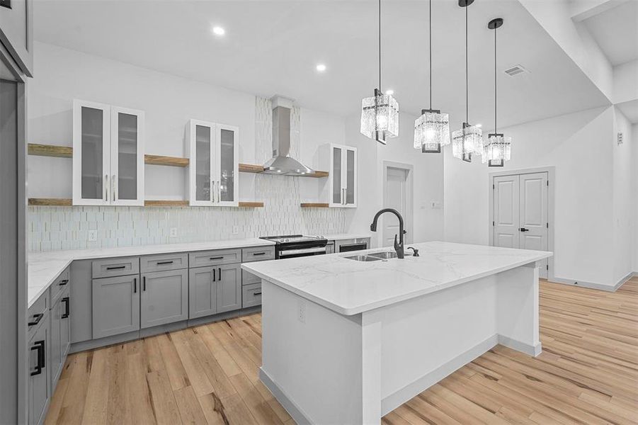 Kitchen with a kitchen island with sink, light hardwood / wood-style floors, sink, a chandelier, and wall chimney range hood