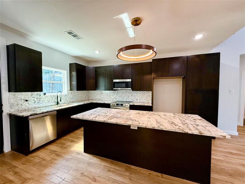 Kitchen with sink, light stone counters, stainless steel appliances, and light hardwood / wood-style flooring