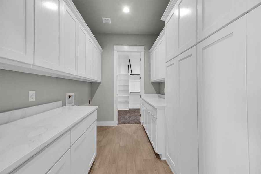 Washroom with light hardwood / wood-style floors, washer hookup, and ample amount of cabinets