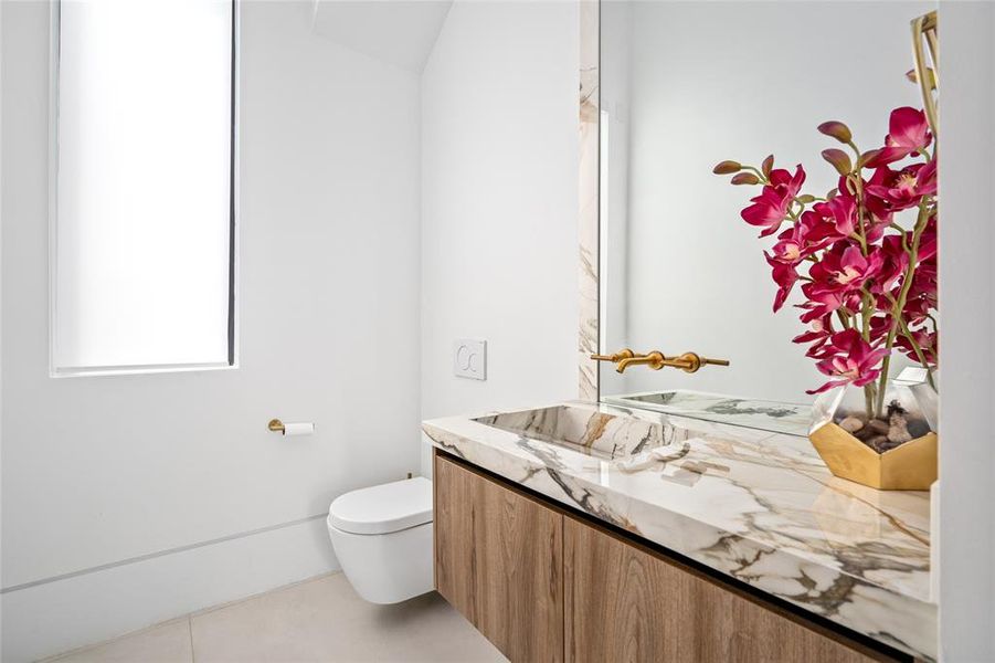 This luxurious first-floor powder room features an elegant vanity with a sleek integrated sink and brushed gold fixtures while the tall, narrow window brings in natural light, creating an open and airy feel.