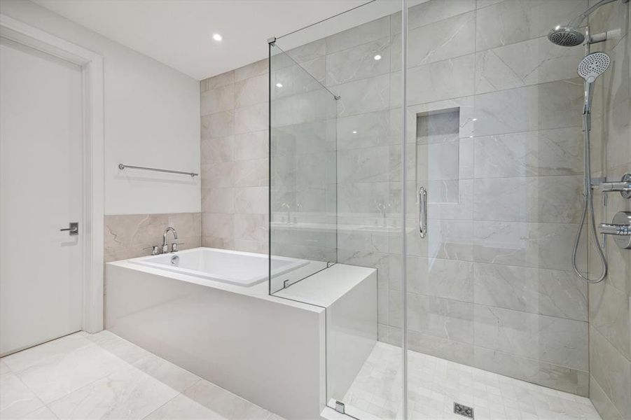 Luxurious soaking bathtub and a separate walk-in shower with bench, shampoo shelf & frameless glass enclosure. It has neutral tiles and is equipped with sleek stainless fixtures.