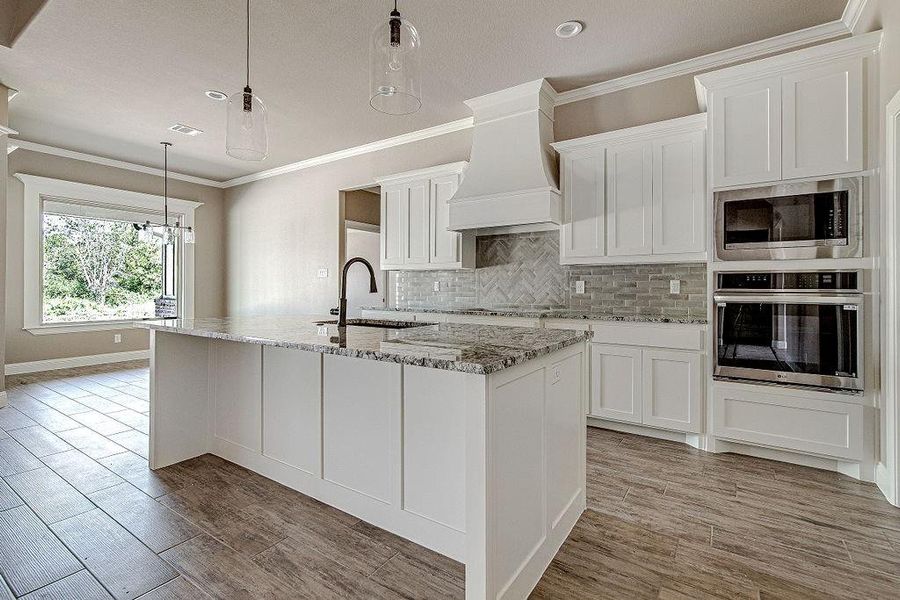 Kitchen featuring premium range hood, tasteful backsplash, stainless steel appliances, sink, and a kitchen island with sink