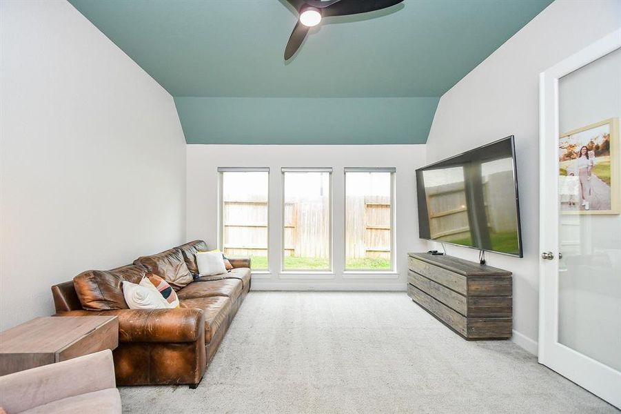 Spacious, well-lit game room featuring a vaulted ceiling with a contrasting paint accent, large windows providing ample natural light, double doors with glass accent. New carpet creates a clean, inviting space. a ceiling fan.