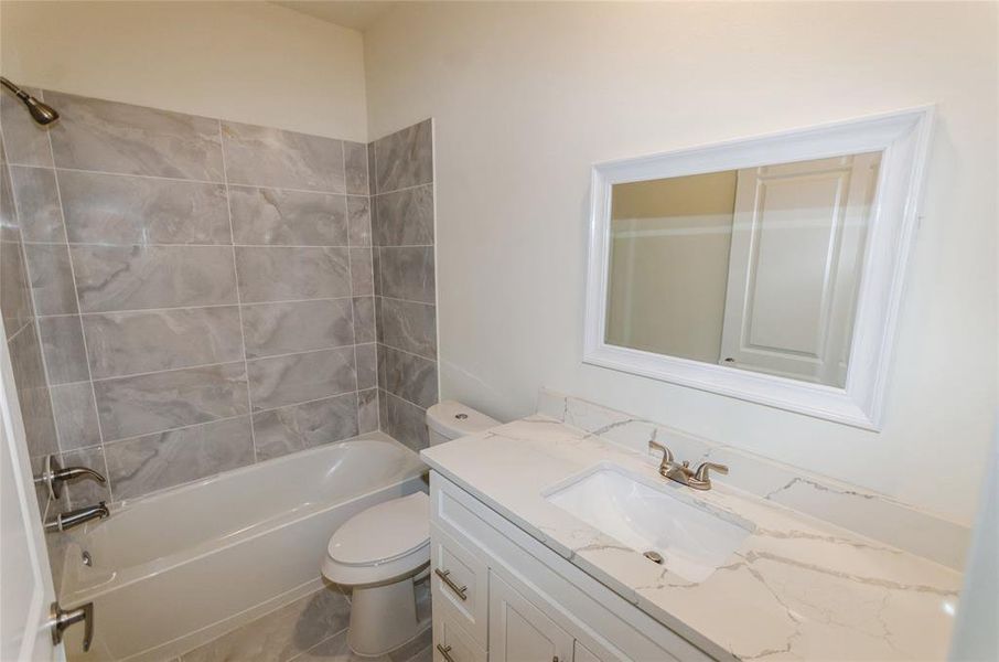 Full bathroom featuring tile flooring, toilet, tiled shower / bath, and vanity with extensive cabinet space