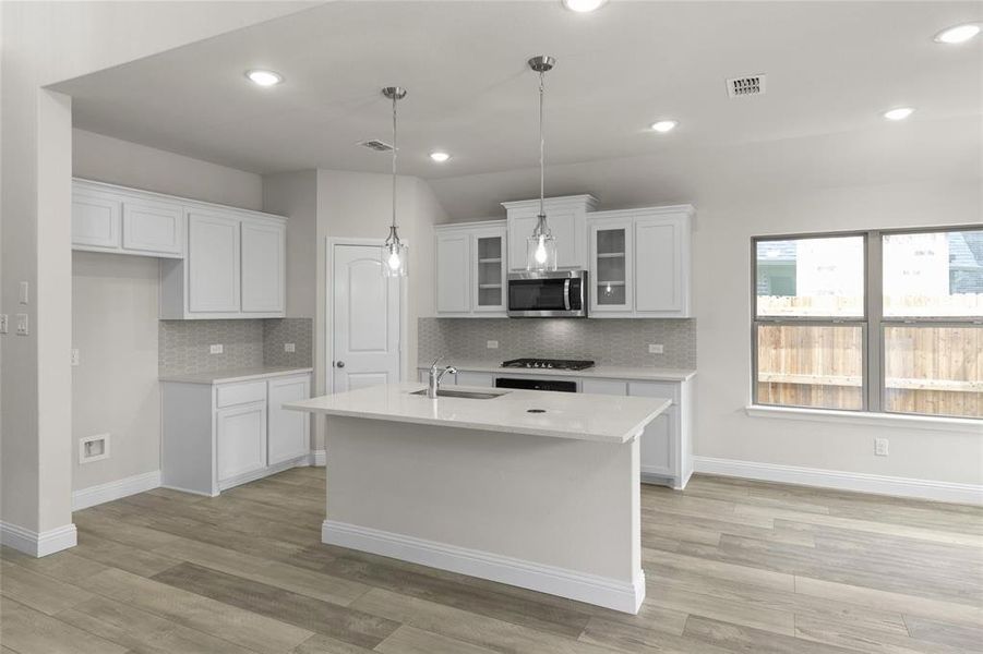 Kitchen with an island with sink, light hardwood / wood-style floors, white cabinets, and tasteful backsplash