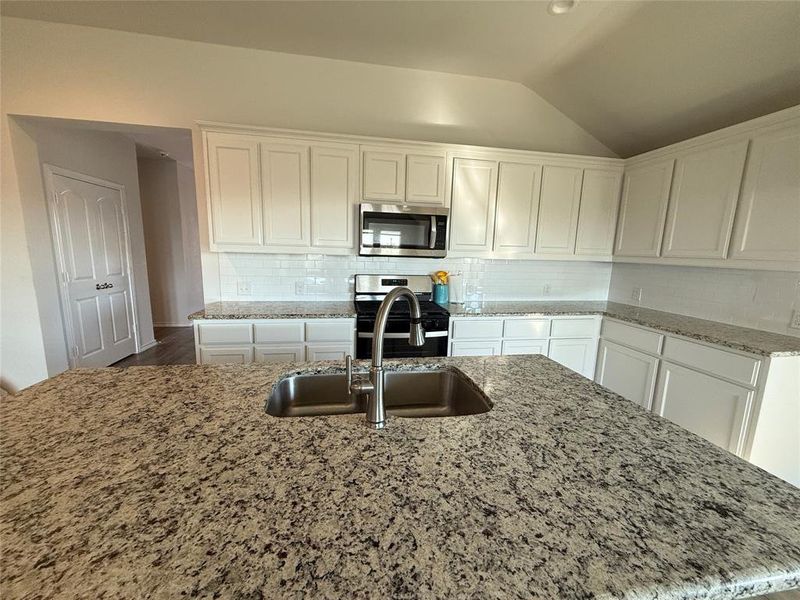 Kitchen with stainless steel appliances, backsplash, lofted ceiling, a kitchen island with sink, and white cabinets