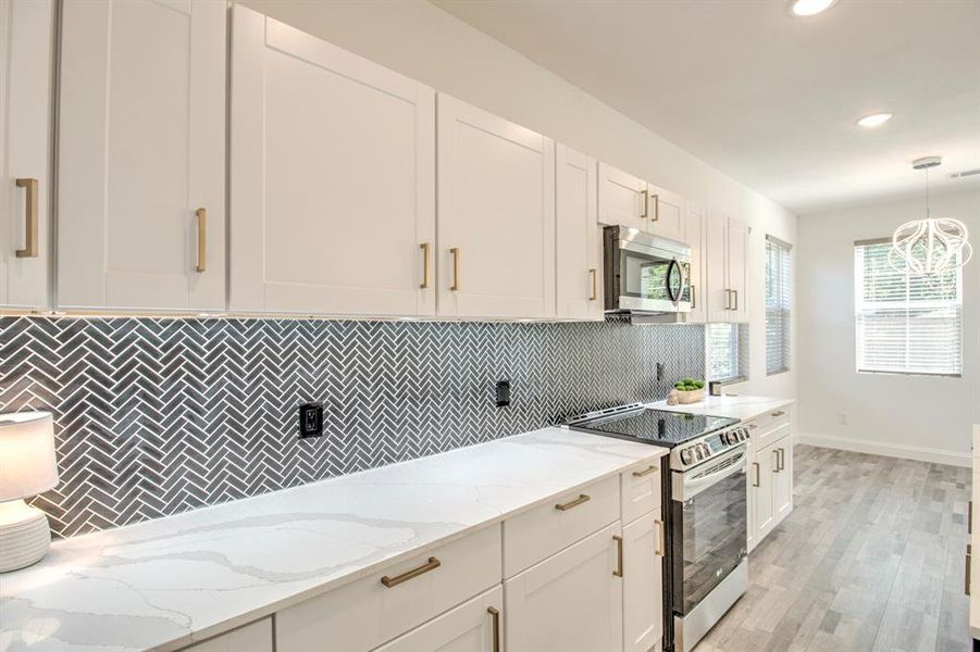 Kitchen with decorative backsplash, appliances with stainless steel finishes, pendant lighting, and white cabinets