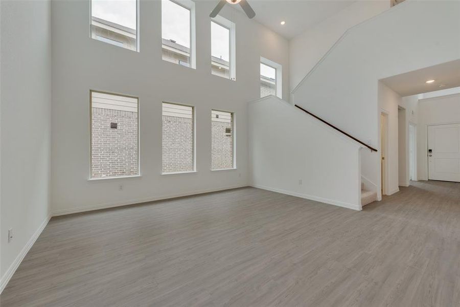 Unfurnished living room with a high ceiling, light hardwood / wood-style floors, and ceiling fan