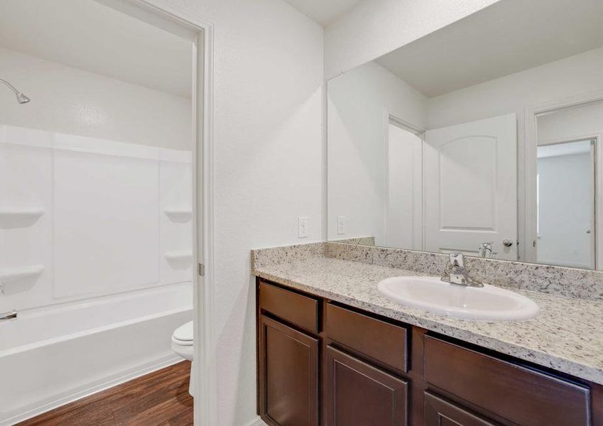 The Rio model home's second bathroom with granite countertops, dark brown cabinetry and shower and tub combo