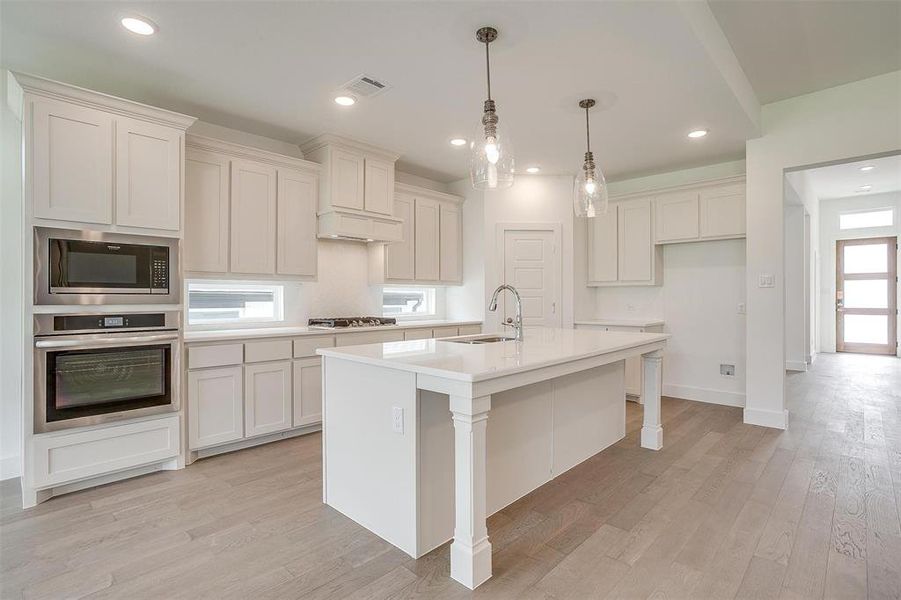 Kitchen with appliances with stainless steel finishes, light hardwood / wood-style floors, a healthy amount of sunlight, and a center island with sink