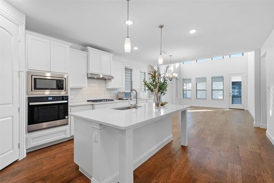 Kitchen featuring stainless steel appliances, decorative light fixtures, a center island with sink, and dark hardwood / wood-style flooring