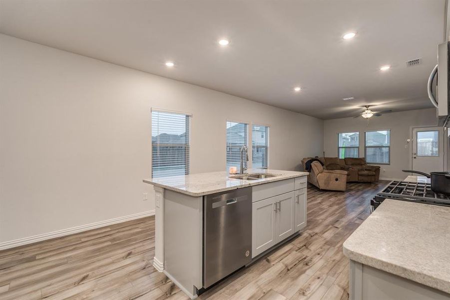 Kitchen with white cabinetry, an island with sink, dishwasher, light hardwood / wood-style flooring, and sink