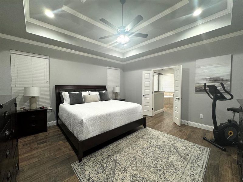 Bedroom with ceiling fan, crown molding, a tray ceiling, tile wood-look floors, and ensuite bath