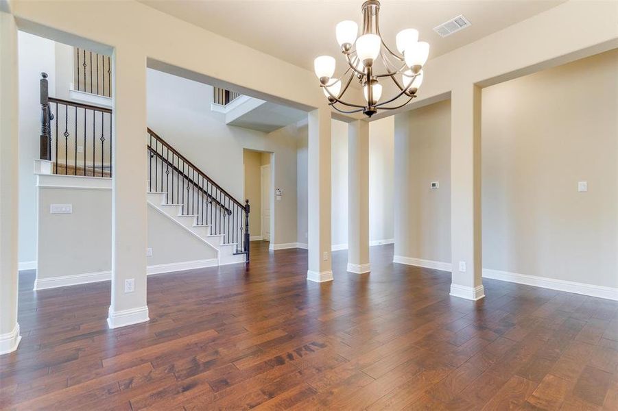 Empty room featuring an inviting chandelier, dark wood-type flooring, and ornate columns