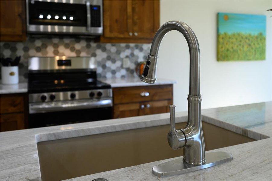 Kitchen with appliances with stainless steel finishes, light stone countertops, and backsplash