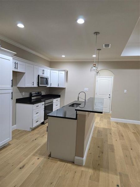 Kitchen with light hardwood / wood-style floors, white cabinetry, stove, decorative light fixtures, and sink