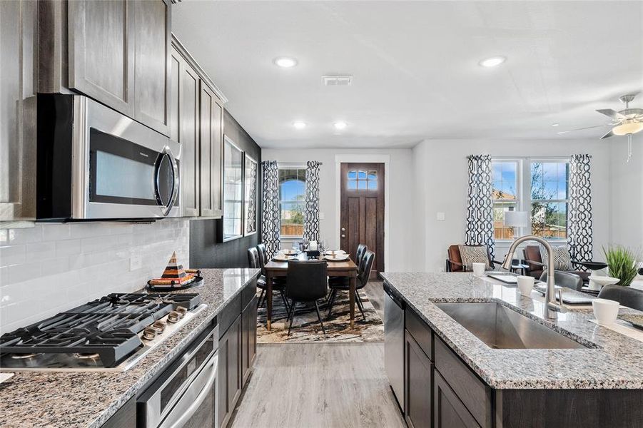 Kitchen with sink, light stone countertops, ceiling fan, appliances with stainless steel finishes, and light hardwood / wood-style floors