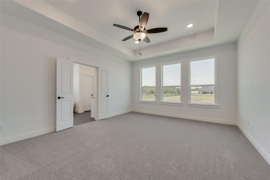 Unfurnished bedroom featuring carpet floors, ceiling fan, and a raised ceiling