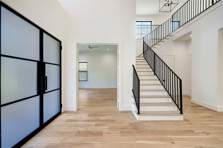 SAMPLE - Light-filled foyer features dramatic, soaring ceiling. View toward the study and the custom wrought iron staircase with solid oak treads. Gorgeous wide plank, natural finish, engineered wood floors throughout.