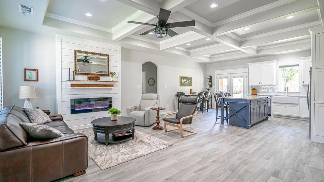 Living room with a large fireplace, light hardwood / wood-style floors, ceiling fan, and coffered ceiling