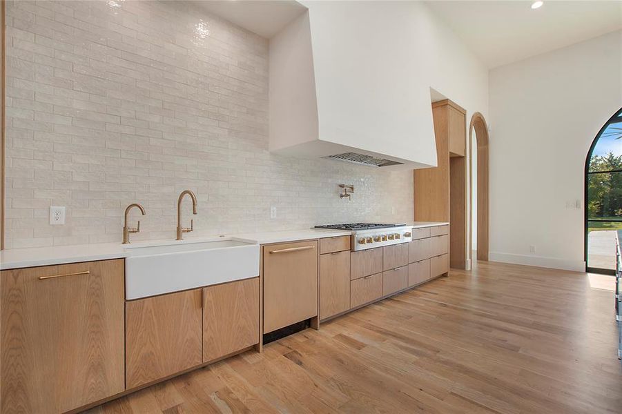 Kitchen with premium range hood, sink, stainless steel gas stovetop, light wood-type flooring, and decorative backsplash