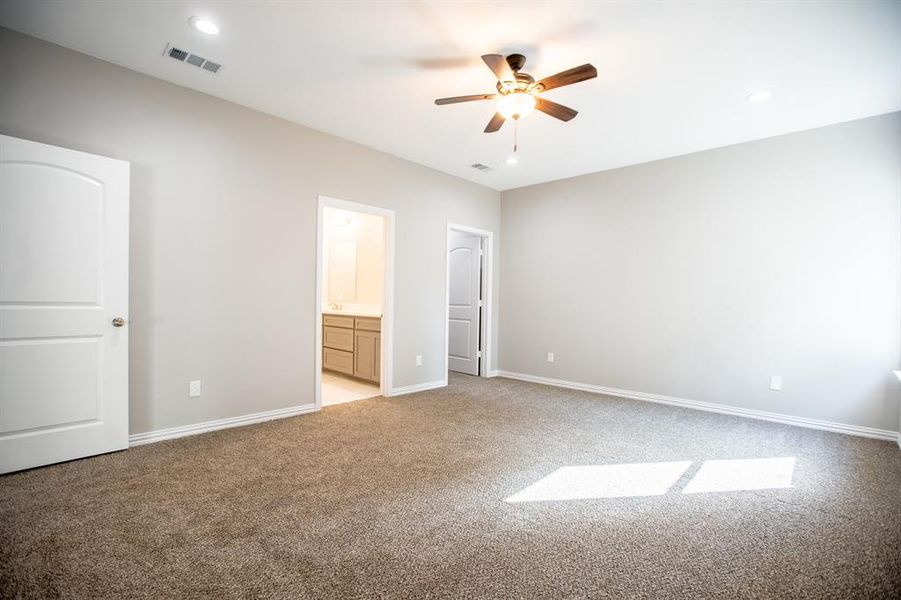 Unfurnished bedroom featuring light carpet, ensuite bathroom, and ceiling fan