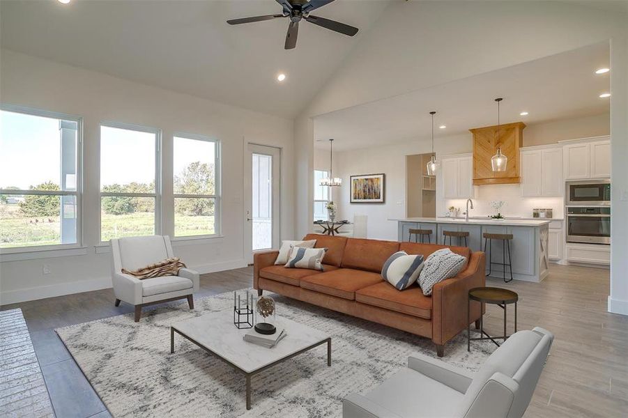 Living room with sink, ceiling fan with notable chandelier, light wood-type flooring, and high vaulted ceiling