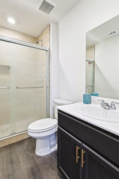 Bathroom featuring wood-type flooring, vanity, toilet, and a shower with door