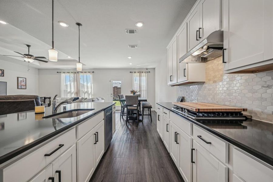 Kitchen featuring dark wood-type flooring, cooktop, white cabinets, sink, and pendant lighting