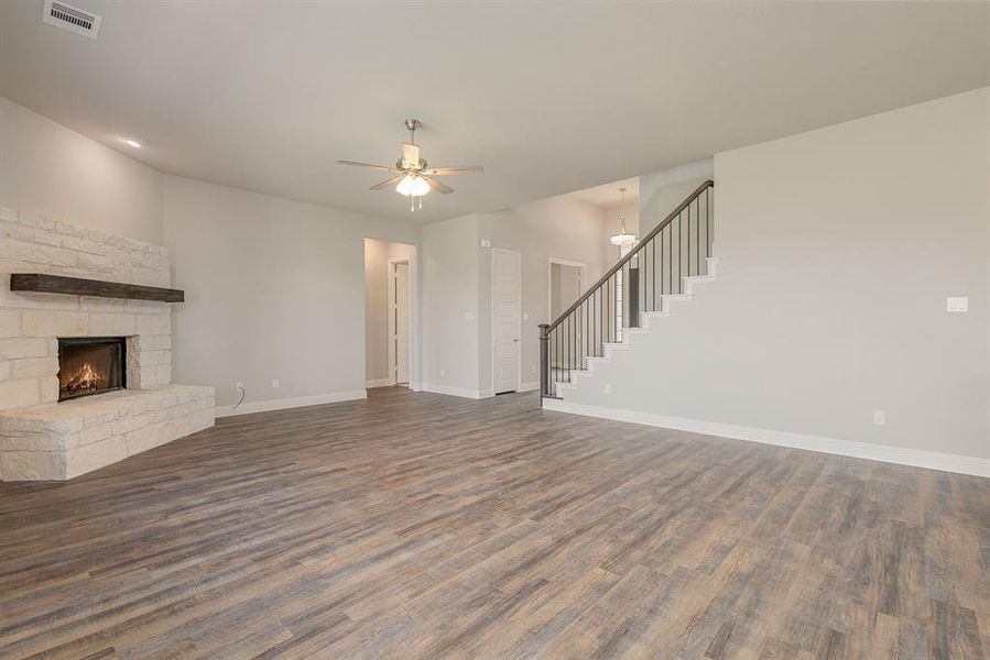 Unfurnished living room featuring ceiling fan with notable chandelier, dark wood-type flooring, and a stone fireplace